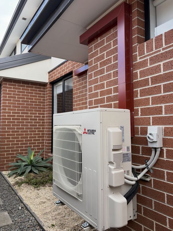 Mitsubishi Electric split system outdoor unit on a brick wall with red Colorbond pipe capping and a weatherproof isolator